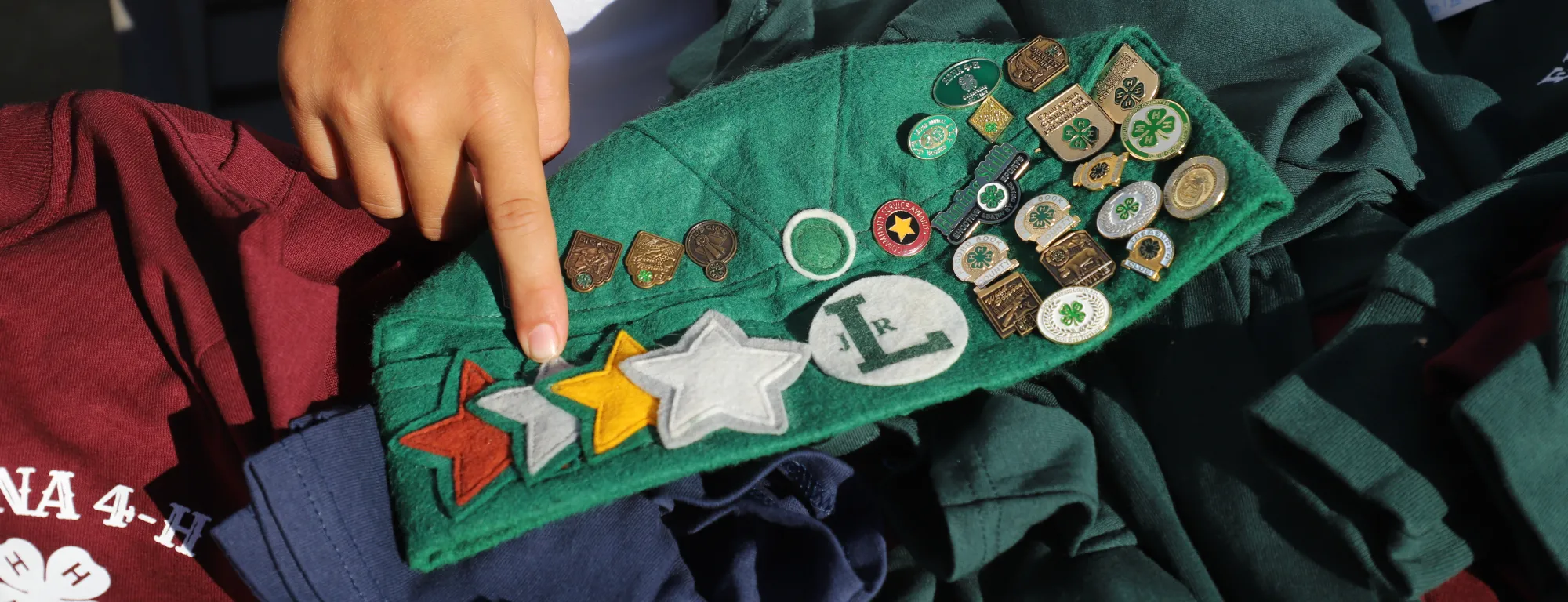 Someone points to the pins and badges on a 4-H hat.