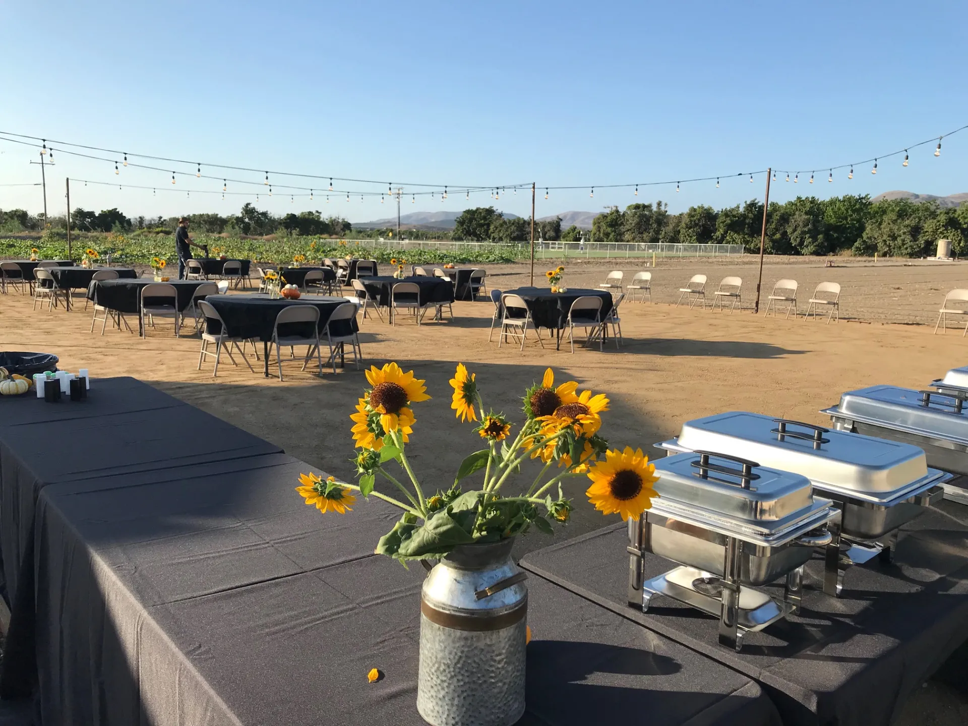 outdoor annex area set up with round tables and chairs, and buffet style food set up, with string lights and flowers for an event
