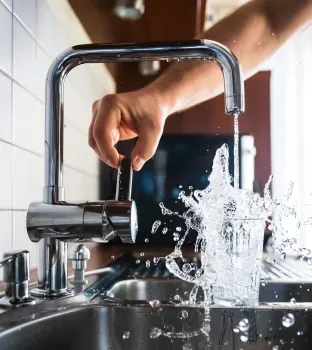 Persona abriendo llave del grifo y el agua saliendo del grifo