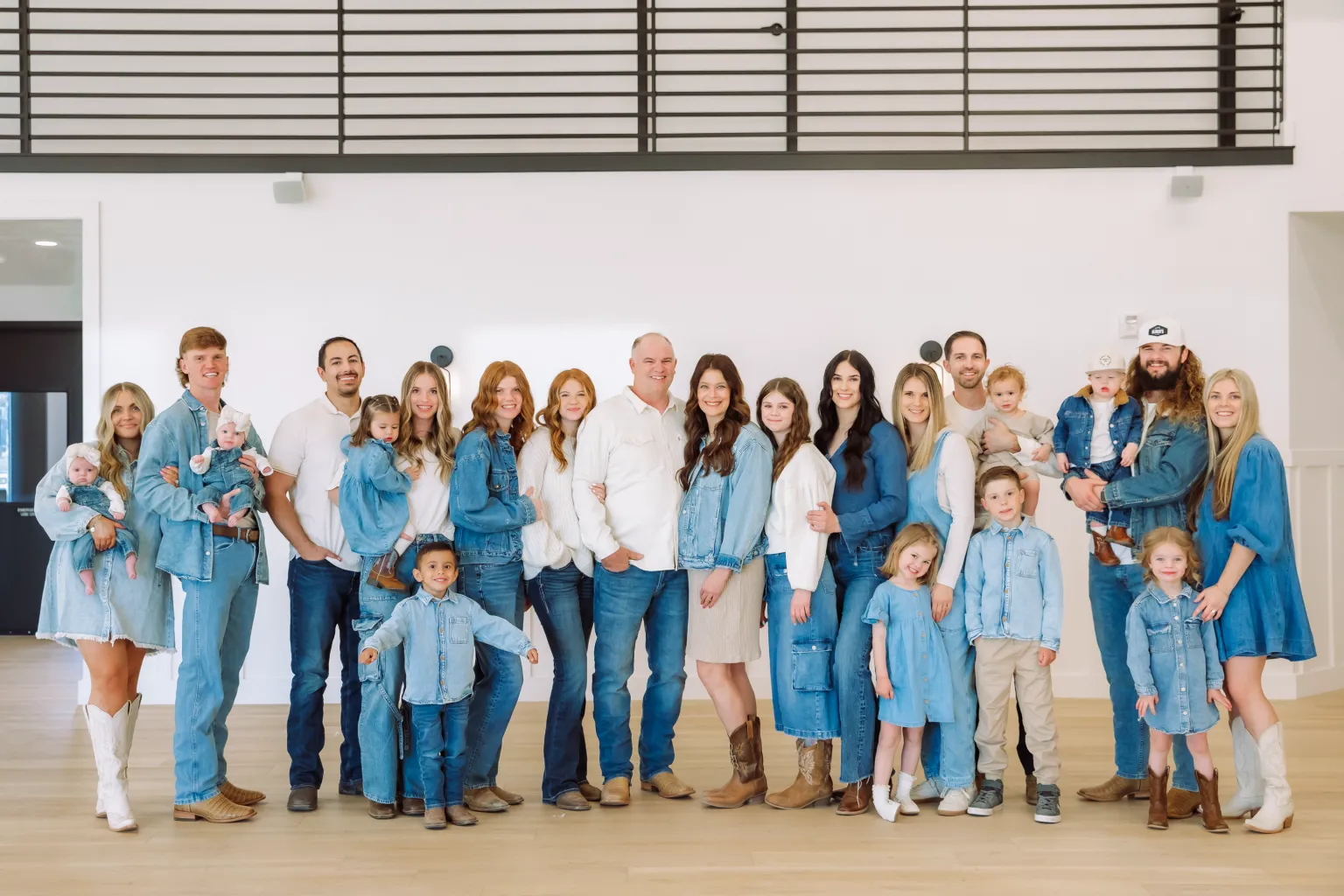 Against a white wall, a family of 23 adults and kids poses dressed in white and denim