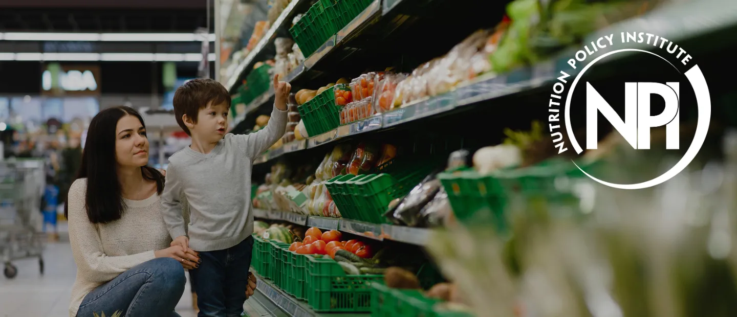 A woman with her young child standing in the produce aisle picking out vegetables. The Nutrition Policy Institute logo is on the right.