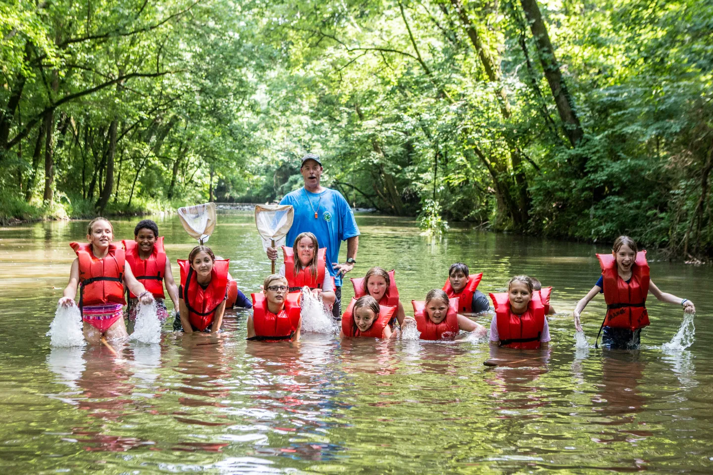 Adult with youth in lifejackets in river, holding nets