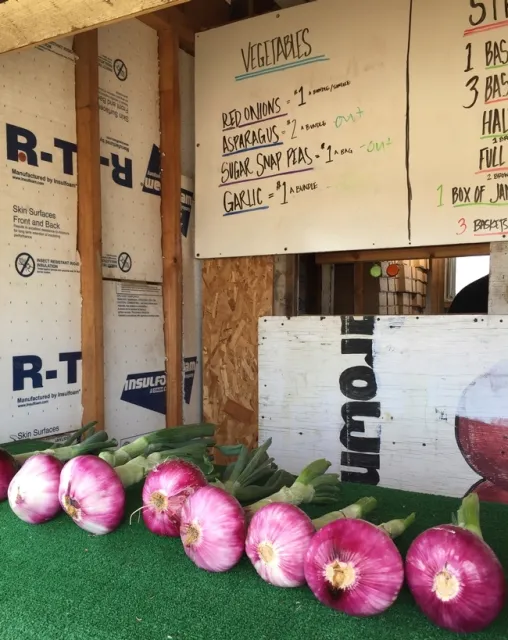 Algunos puestos de granjeros ofrecen verduras, como estas cebollas moradas, para complementar la venta de fresas.