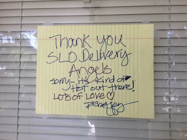 A sign taped on a window with blinds in the background that reads. Thank you SLO Deivery Angels, Sorry-it's kind of hot out there! Lots of Love.