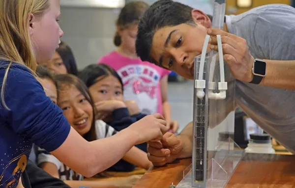 Girls peer into a plexiglass frame filled with soil to watch water flow through the soil