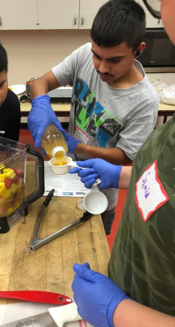A Teens Love Cooking student measuring ingredients to make a smoothie