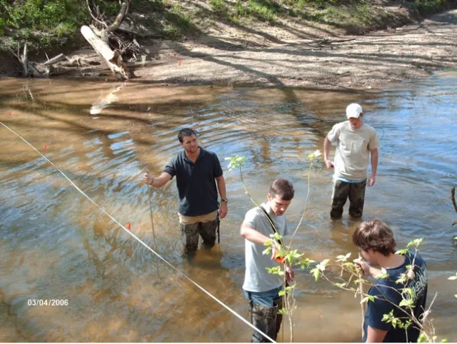 Four men stand in water, attempting to take measurements.
