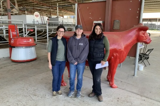 De izquierda a derecha: Fernanda Ferreira, ex investigadora de la Facultad de Veterinaria de UC Davis, Shonda Reid, gerente de la lechería Fred Rau y Daniela Bruno, asesora de lecherías de Extensión Cooperativa de UC, quien ha colaborado en estudios sobre lecherías grandes en California que usan los sistemas de ordeño automatizados. A la distancia se observa un robot que empuja alimento hacia las vacas. Fotografía cortesía de Daniela Bruno