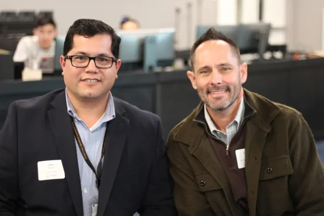 Two middle aged men smile at the camera.