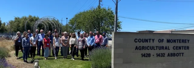 A group of a couple dozen people pose outdoors next to the 