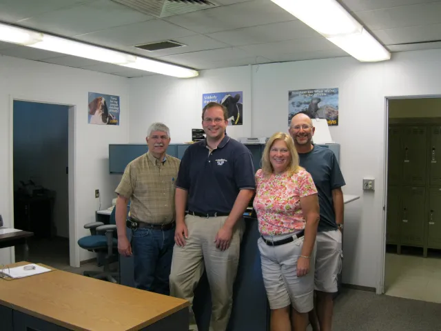 Four people stand in a row in an office