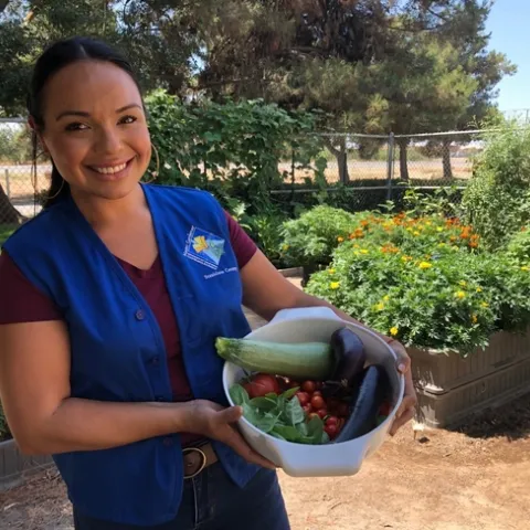 Smiling woman wearing a blue vest standing in a garden.