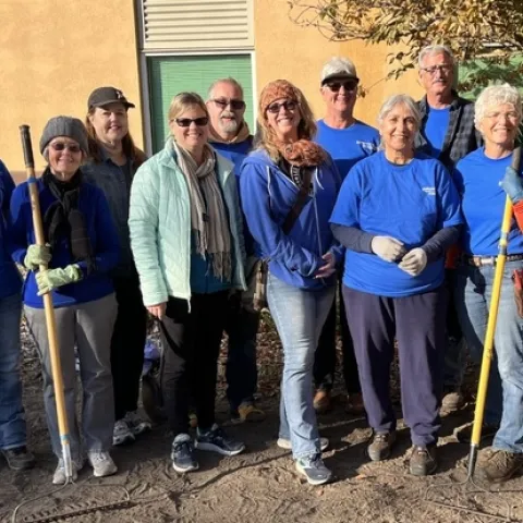 Smiling group of people, standing in two rows while holding gardening tools.