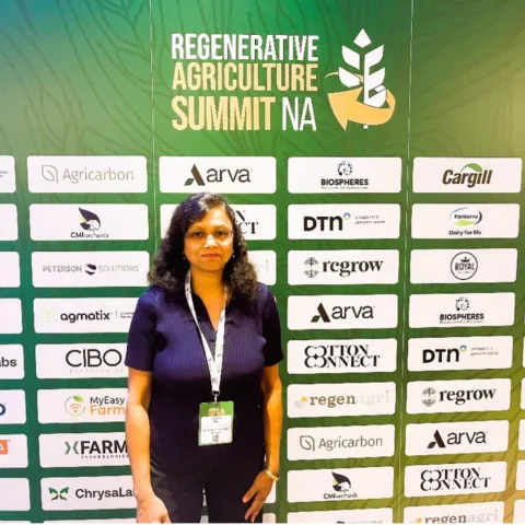 Srabani Das stands in front of a banner for Regenerative Agriculture Summit NA with sponsor logos. 