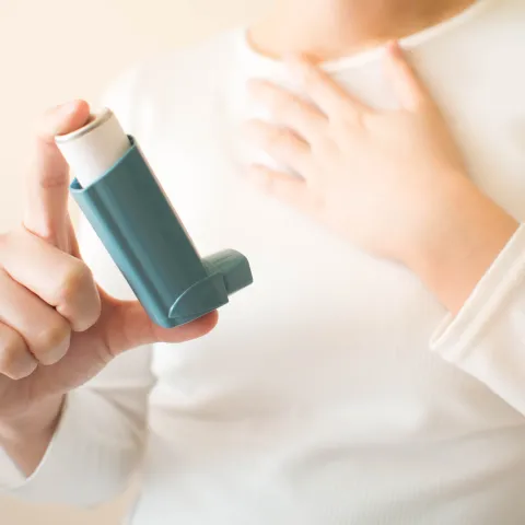 A person holding an inhaler in their hand and clenching their chest.