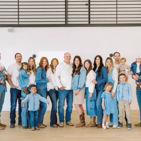 Against a white wall, a family of 23 adults and kids poses dressed in white and denim