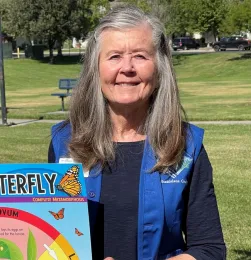 Master Gardener wearing a blue vest holding a butterfly life cycle sign.