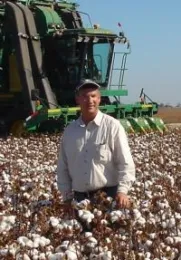 Munk stands in a field of cotton ready for harvest, with a green cotton harvester in the background.