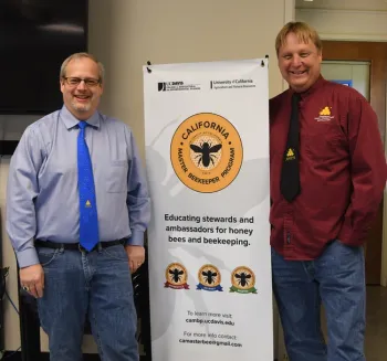 Kelvin Adee (left) of Bruce, S.D., president of the American Honey Producers' Association, and past president Darren Cox of Logan, Utah, stand by a California Master Beekeeper Program banner in the Harry H. Laidlaw Jr. Honey Bee Research Facility, UC Davis. (Photo by Kathy Keatley Garvey)