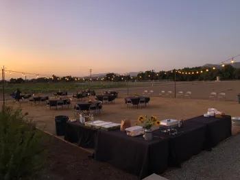 A sunset view of the outdoor annex area set up with round table and chairs and buffet, with string lights and flowers, for an event