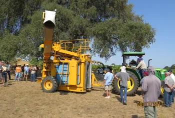 A group of farmers looking at a stationary mechanical grape harvester.