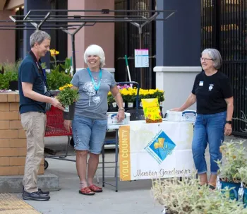 UC Master Gardener Volunteers working a table at a garden center talking with a community member.