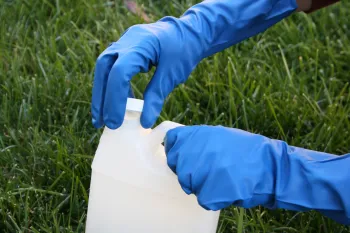 A person wearing blue gloves on their hands is unscrewing the cap to a white container