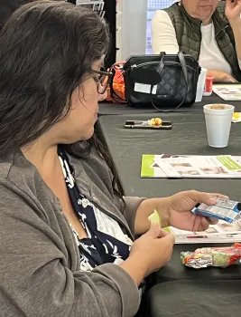 Adult EFNEP participant eating an apple slice while reading the nutrition facts on a snack bar label.