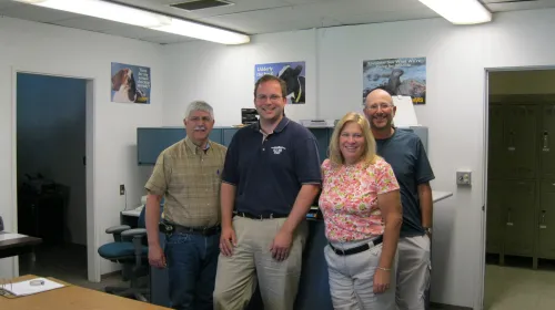 Four people stand in a row in an office