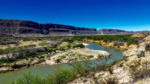 The Rio Grande River winds through a desert landscape with green shrubs