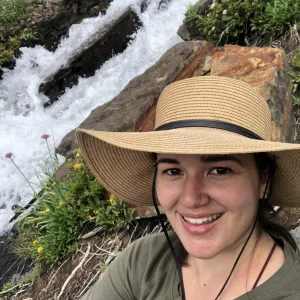 Photo of a woman in a broad sun hat. In the background is a rushing waterfall.